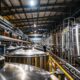 a bustling factory interior showcasing large stainless steel tanks and gleaming machinery, where workers meticulously oversee the production of rich, golden syrup under bright industrial lighting.